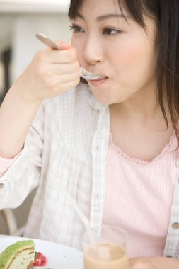 Kafede tatlı yiyen mutlu Asyalı genç kadın.