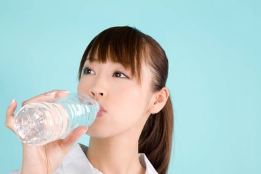 Güzel genç Asyalı kadın mavi arka planda izole edilmiş su içiyor.