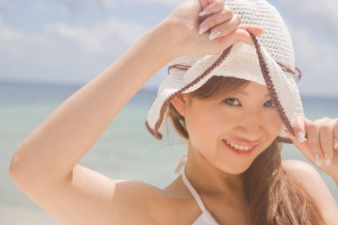 Genç Asyalı kadın yaz plajında şapka takıyor.
