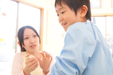 Anaokulunda kille oynayan Asyalı küçük çocuk ve genç kadın.