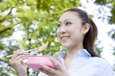 Genç Japon kadın yaz parkında oturmuş yemeğin tadını çıkarıyor. 