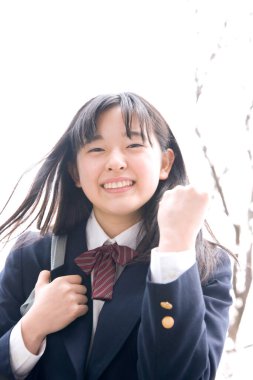 Çiçek açan kiraz ağacının arka planında yumruğunu gösteren güzel Japon okul kızının portresi.