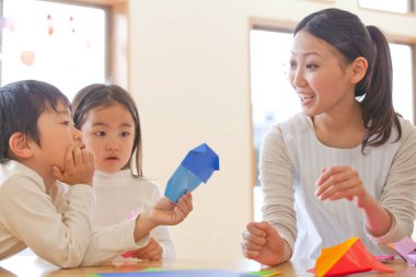 Genç bayan öğretmen ve sevimli Asyalı küçük çocuklar Japon anaokulunda kağıt origami yapıyorlar.