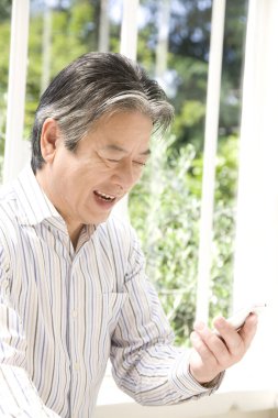 Evde akıllı telefon kullanan yakışıklı, olgun bir Japon 'un portresi.