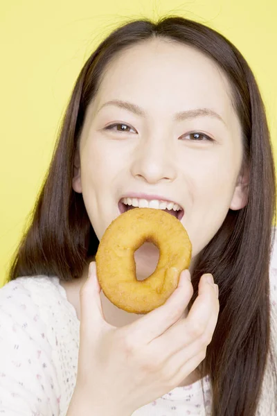 年轻的亚洲女人在吃甜甜圈 — 图库照片