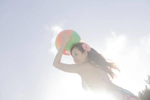 Pretty Japanese woman in swimsuit resting on beach at daytime, summer vacation concept