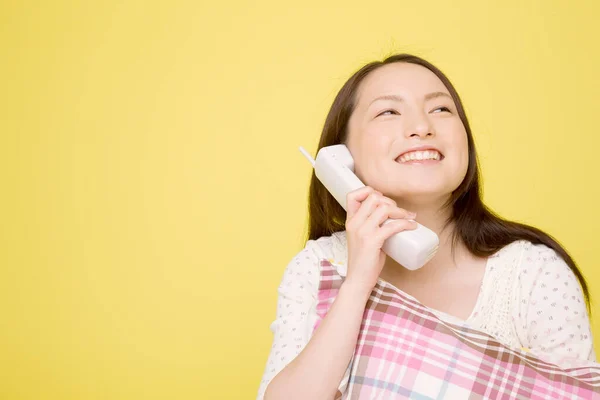 ピローを持ち 黄色の背景に隔離された電話で話す美しい日本の女性の肖像画 — ストック写真