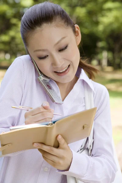 Όμορφη Χαρούμενη Νεαρή Ασιατική Γυναίκα Κρατώντας Σημειωματάριο Και Μιλώντας Από — Φωτογραφία Αρχείου