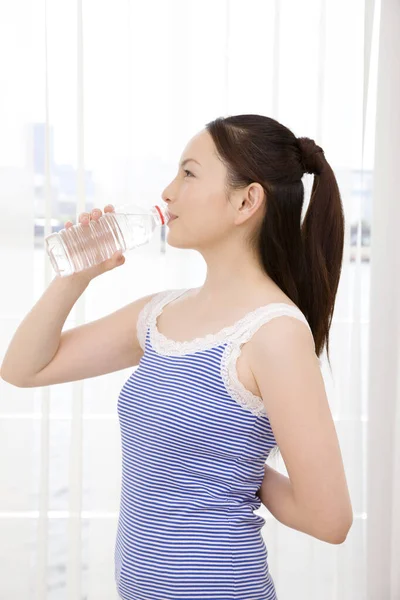 漂亮的年轻亚洲女人在家里用瓶子喝水 — 图库照片