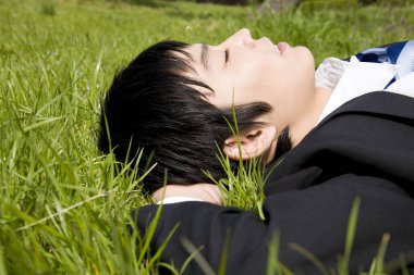 İş adamı çimenlerin üzerinde gözleri kapalı yatıyor.