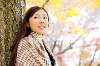 Güzel Asyalı kadın sonbahar parkında geziniyor.