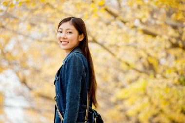 Güzel Asyalı kadın sonbahar parkında geziniyor.