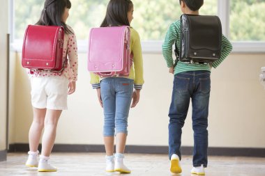 Okul koridorunda sırt çantalı bir grup Asyalı öğrenci.