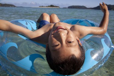 Mavi elbiseli küçük Asyalı çocuk. Can simidi. Deniz dalgalarının tadını çıkarıyor.