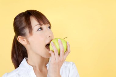 Yeşil elma yiyen genç bir kadın, sarı arka planda izole edilmiş.