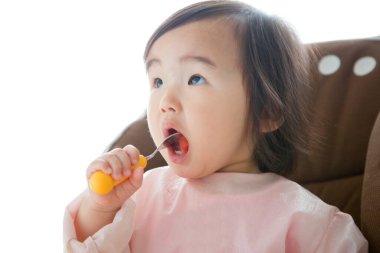 Bebek turuncu saplı kaşıkla yemek yiyor.