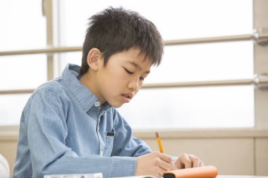 Çocuk masadaki sınıfta yazıyor.