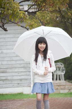 Sırt çantası ve şemsiyeli Asyalı kız okula gidiyor. 