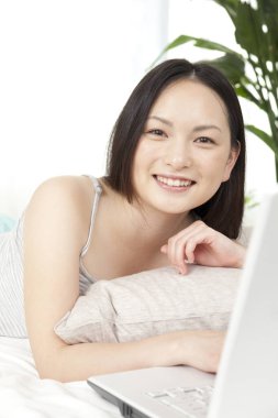 Güzel genç Asyalı kadın yalan söylüyor ve evinde dizüstü bilgisayar kullanıyor.