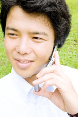 Yaz parkında cep telefonuyla konuşan genç Asyalı adam.