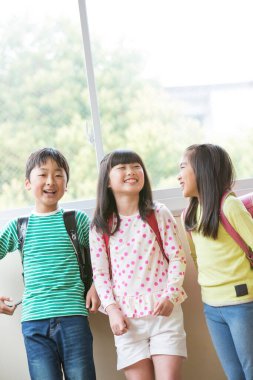 Okul koridorunda sırt çantalı bir grup Asyalı öğrenci.