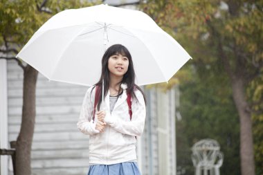 Sırt çantası ve şemsiyeli Asyalı kız okula gidiyor. 