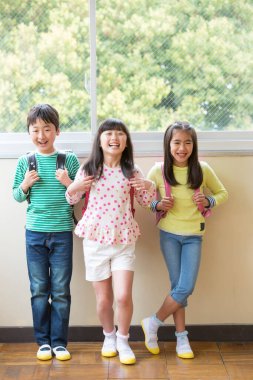 Okul koridorunda sırt çantalı bir grup Asyalı öğrenci.