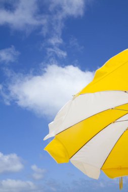 Mavi gökyüzüne karşı sarı ve beyaz çizgili plaj şemsiyesi