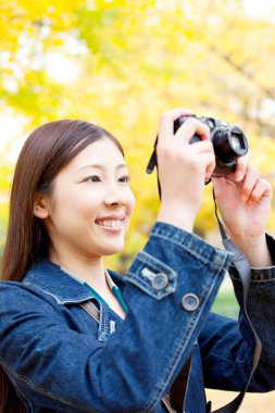 Genç bir kadın parkta kamerayla fotoğraf çekiyor.
