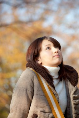 Genç güzel Asyalı kadın sonbahar parkında poz veriyor.