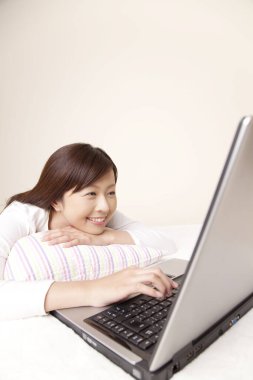 Gülümseyen kadın yastıkla yatıyor ve dizüstü bilgisayar kullanıyor. 