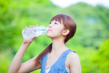 Genç Asyalı kadın parkta su içiyor. 