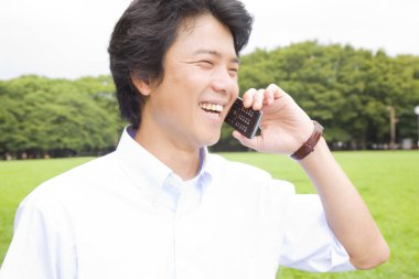 Yaz parkında cep telefonuyla konuşan genç Asyalı adam.