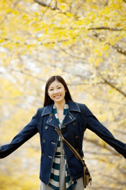 Güzel Asyalı kadın sonbahar parkında geziniyor.