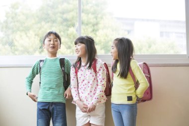 Okul koridorunda sırt çantalı bir grup Asyalı öğrenci.