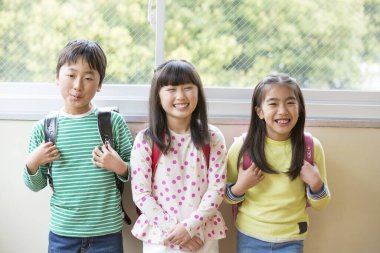 Okul koridorunda sırt çantalı bir grup Asyalı öğrenci.