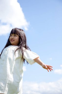 Mutlu küçük Asyalı kız mavi gökyüzüne karşı yeşil çayırda poz veriyor.