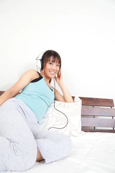 Güzel Genç Asyalı Bir Kadın Yatakta Uzanıp Kulaklıkla Müzik Dinliyor — Stok fotoğraf