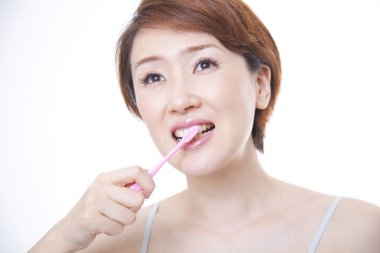 Güzel Asyalı kadın diş fırçasıyla diş temizliyor.
