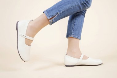 Kadın bacakları beyaz ayakkabılar ve açık arkaplanda kot pantolon giyiyor. 