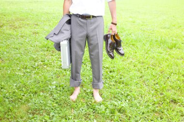 Gri takım elbiseli ve parktaki çimlerin üzerinde çıplak ayakla duran iş adamının kesilmiş fotoğrafı.