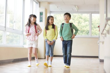 Okul koridorunda sırt çantalı bir grup Asyalı öğrenci.