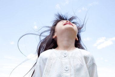 Mutlu küçük Asyalı kız mavi gökyüzüne karşı yeşil çayırda poz veriyor.