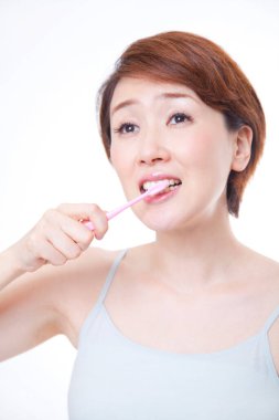 Olgun Japon kadın beyaz arka planda dişlerini fırçalıyor.