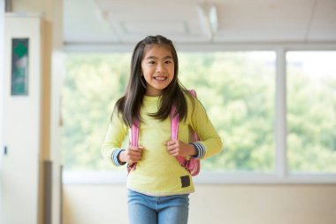 Okulun koridorunda sırt çantalı Asyalı bir kızın portresi.