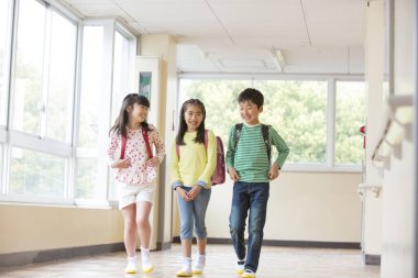 Okul koridorunda sırt çantalı bir grup Asyalı öğrenci.