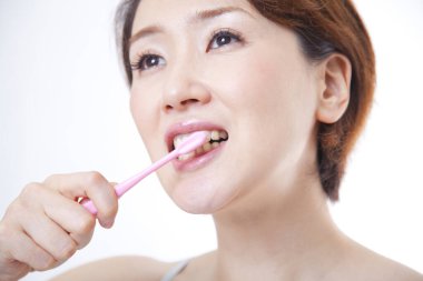 Beyaz arka planda dişlerini fırçalayan Asyalı kadın. 