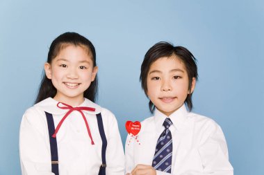 Elinde kalp şeklinde lolipop tutan gülümseyen çocuklar.