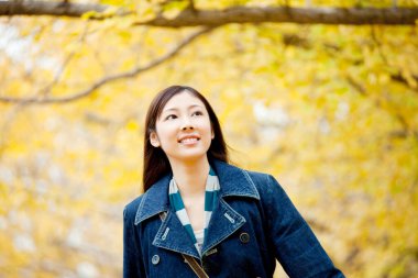 Güzel Asyalı kadın sonbahar parkında geziniyor.