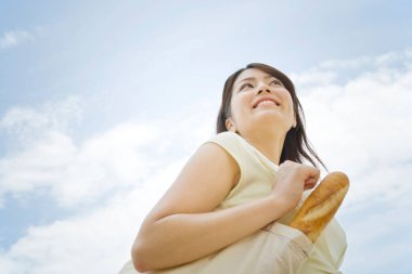 Kadın çantasında ekmeği gökyüzüne karşı tutuyor.